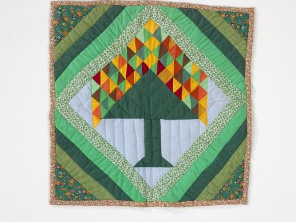 Quilt with a central tree motif with colorful diamond leaves set in a diamond pattern