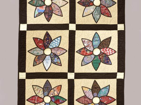 Quilt with six daisies, each petal made of a different patterned fabric, on an off-white background