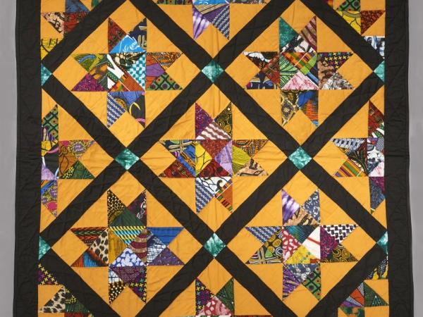 Colorful quilt with golden background, black borders, and African batik and patterned fabrics fabric shaped into stars.