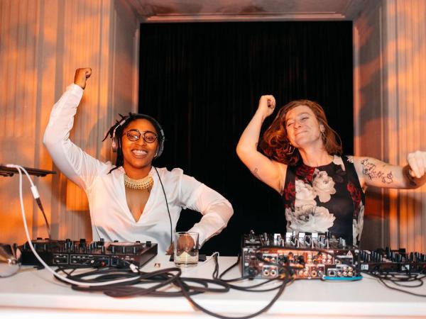 Two women dance in sync at a DJ booth.