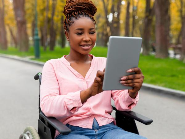 Student sits outside and uses an iPad. She sits in a wheelchair.