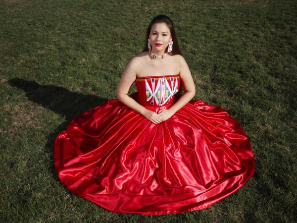 Color photograph of a young women wearing a long, strapless, red satin dress with geometric designs on the bodice.