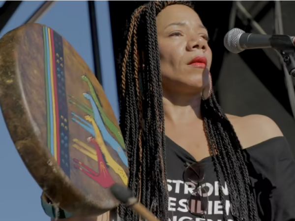 Martha Redbone sings into a microphone and plays a colorful handheld drum.