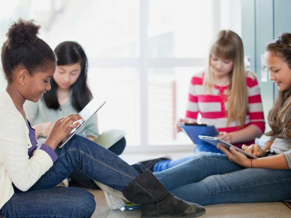 Four girls sit by the lockers, looking tablets.