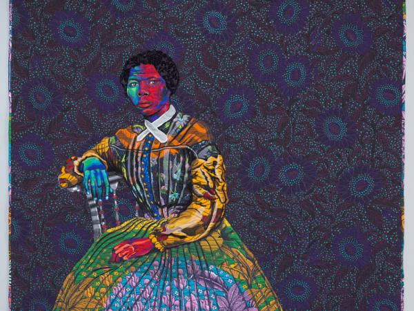 Quilt depicting Harriet Tubman, in multiple bright-colored fabrics, seated against a dark background with a sunflower pattern