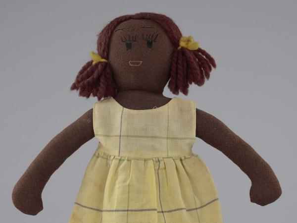 A cloth doll, her hair in pigtails, wearing a tan dress with stripes.