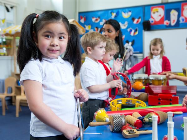 Girl with pigtails looks at camera as her classmates play with musical instruments.