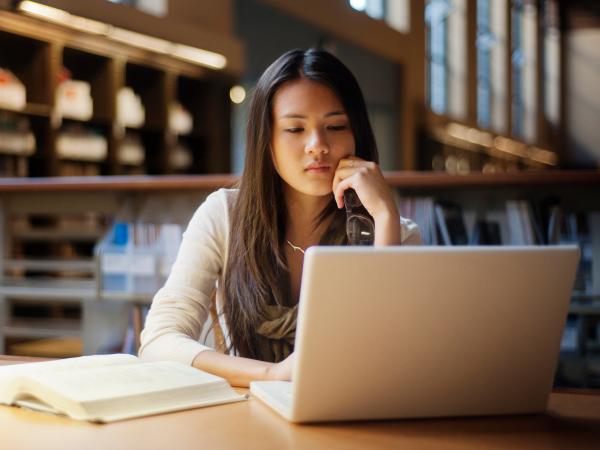 Woman sitting in a library looks at her laptop screen.