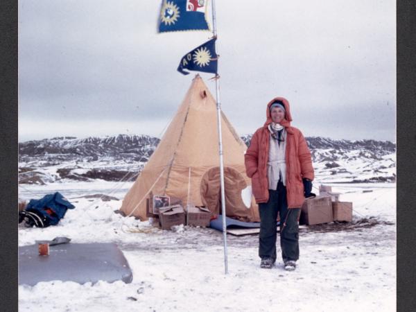 Ursula Marvin stands next to a tent and a flagpole with a Smithsonian sunburst flag in a snowy landscape