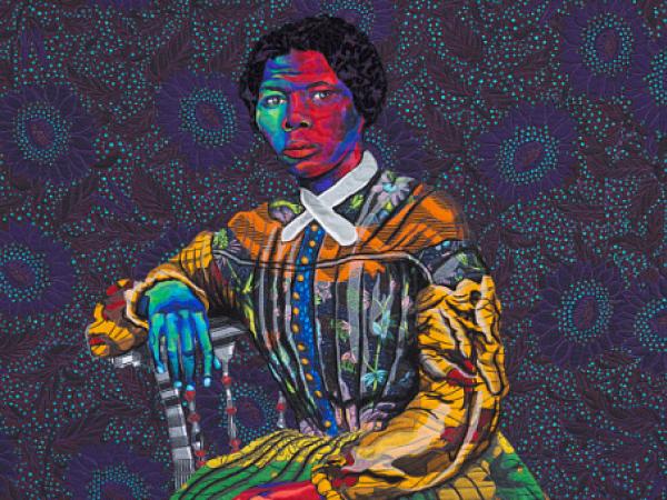 Quilt depicting Harriet Tubman, in multiple bright-colored fabrics, seated against a dark background with a sunflower pattern