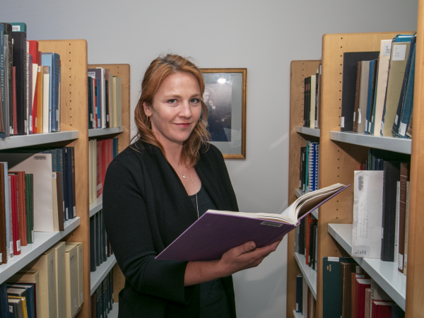 Dr. Elizabeth Harmon opens a book in library stacks.