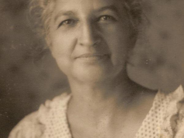  A sepia-toned portrait of Jennie Ross Cobb taken about 1945. She wears a light colored blouse with a v-neck ruffled collar and is smiling softly.