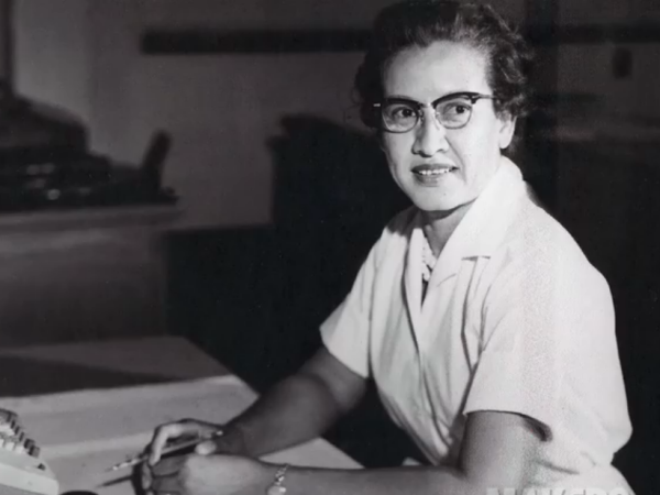 A black and white photo of Katherine Johnson sitting at a desk in front of a typewriter and open notebook.