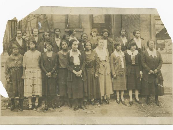 This black and white photograph that depicts twenty-one African American women and one small child. The women stand in two rows on the steps of a building.