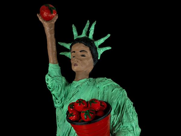 Papier-mache version of the Statue of Liberty. Liberty is Latina and carries a cornucopia of tomatoes instead of a tablet. Instead of a torch, she holds a tomato aloft in her hand.