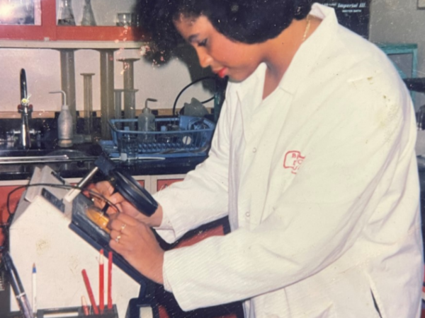 Robin Kumoluyi wears a lab coat and reviews a sample under a magnifying glass