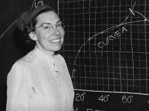 Mary Blade stands smiling in front of a chalkboard with a graph drawn on it