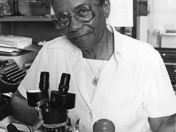 Sophie Lutterlough wears a lab coat and sits in front of a microscope in the Department of Entomology at the National Museum of Natural History.