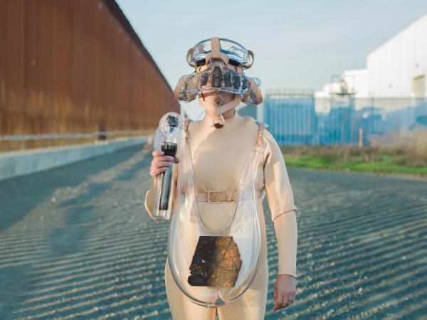 Artist Tanya Aguiñiga wearing a suit made of wearable glass elements at the U.S./Mexico border wall