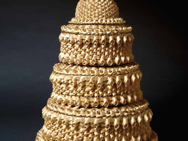 Woven sweetgrass and ash splint baskets stacked to look like a five-tier wedding cake. The top basket features two wedding bells.