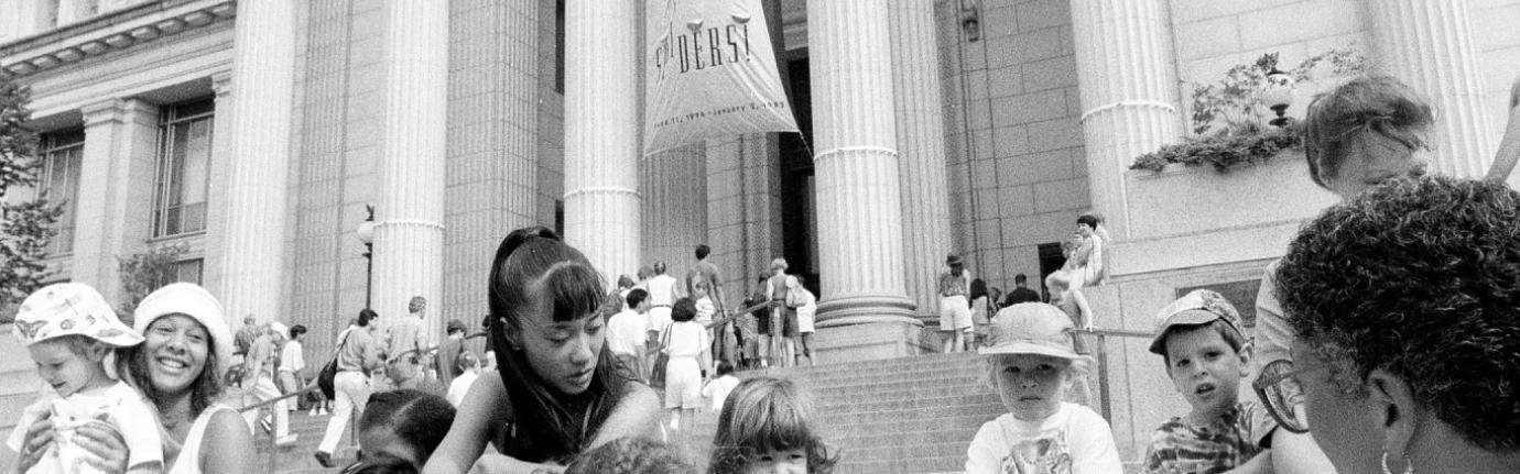 a group of young children and their teacher sitting on steps outside of museum building