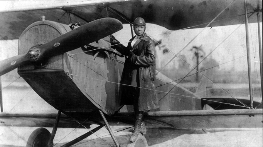  Photo of Bessie standing on the wheel of her airplane in a custom flying suit