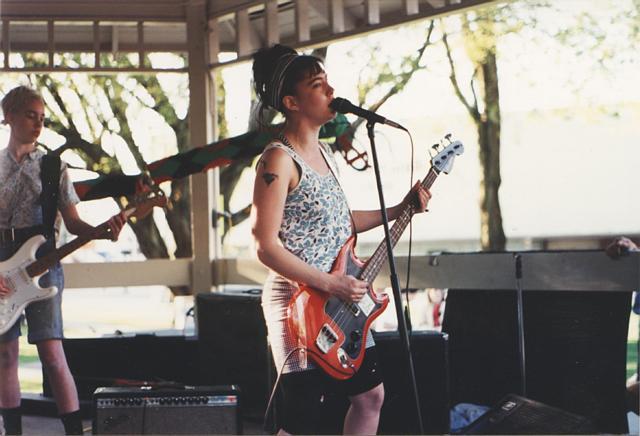 Photo of Kathleen Hanna and bandmate playing guitars in a pavilion