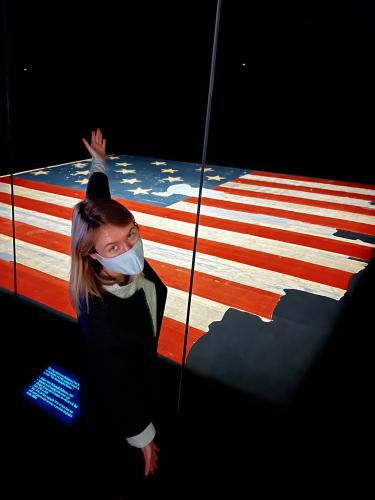 Lizzie Peabody spreads her arms wide in front of the large U.S. flag