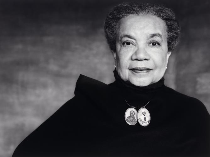 Black and white photograph of Marian Wright Edelman dressed in dark clothing and wearing a necklace with two oval-shaped portraits of Harriet Tubman and Sojourner Truth.