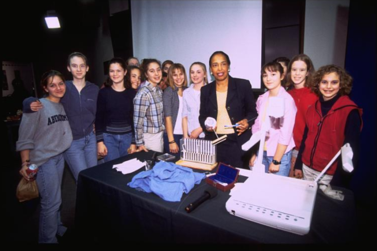 Dr. Patricia Bath holds ophthalmologist tools and posing with a large group of students