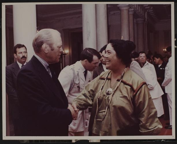 Gerald Ford shakes hands with Grace Thorpe in a crowded room. Thorpe is smiling.