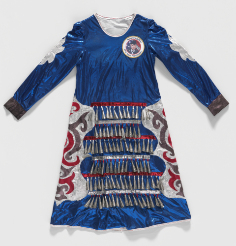 Blue dress made of shiny synthetic fabric with metal bells across the skirt. Above the left breast sits a patch that reads &quot;Never Forgotten SPC Lori Piestewa.&quot;