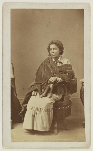 Black and white photograph of Edmonia Lewis sitting in a chair, wearing a velvet fabric drape