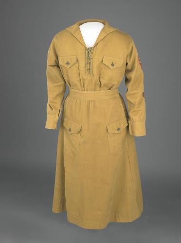 Khaki Girl Scout Uniform consisting of a middy blouse, skirt, and sash/belt. The middy blouse has a lace-up neck line and three patches on the left arm.