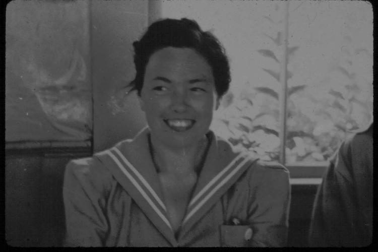 A young Marian Pettibone with dark hair and a 1940’s style dress smiles at something off-camera. 