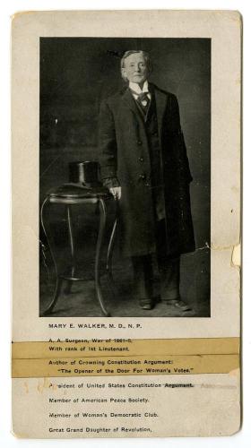 Dr. Mary Walker stands, leaning on a cane, next to a top hat. She wears a suit and glasses. 