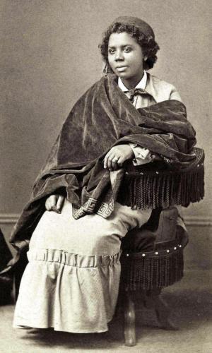 Edmonia Lewis, seated on a chair with tassels. 