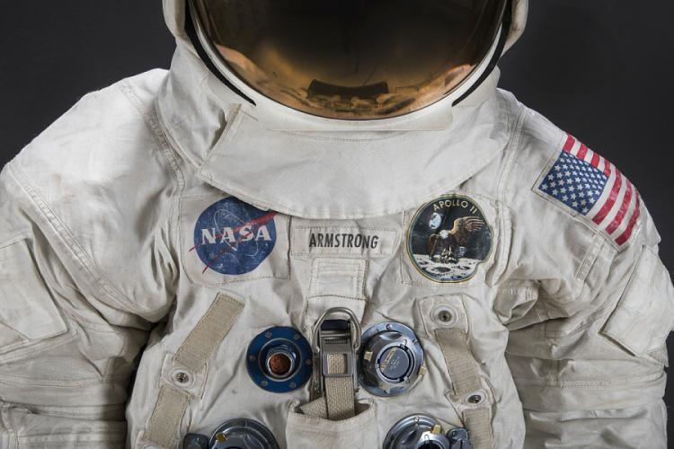 Color photograph of the upper torso and neck of Neil Armstrong's Apollo 11 spacesuit. A NASA patch is on the left and an Apollo 11 patch with an eagle on the moon is on the right.