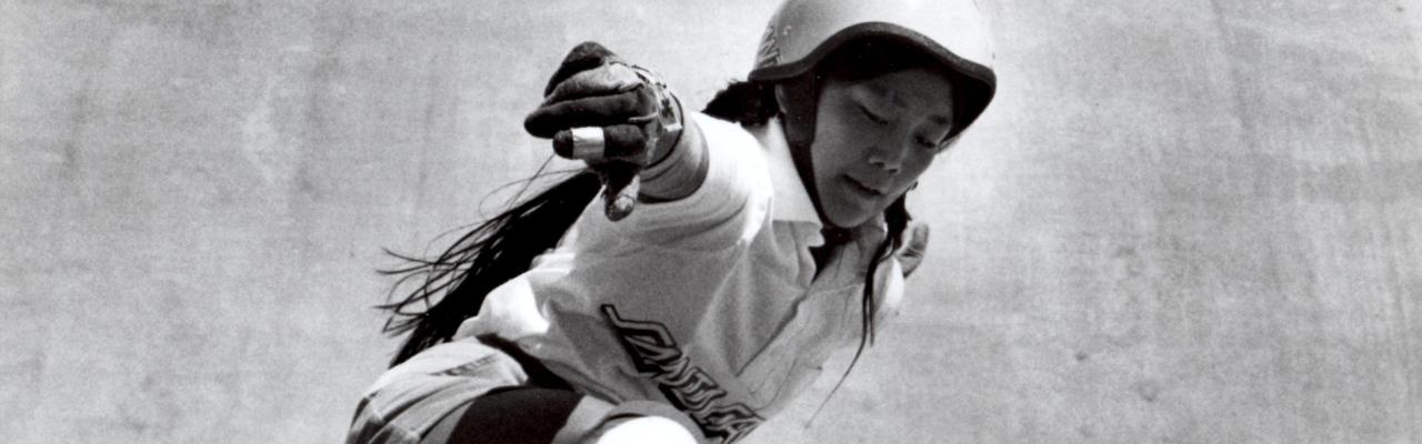 Judi Oyama crouched while riding a skateboard